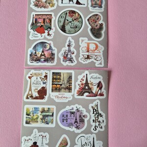 May include: Two sheets of stickers featuring Parisian themes. Designs include the Eiffel Tower, vintage cars, clocks, high heels, and illustrations of people. The stickers have a variety of colors, including pink, red, and brown.