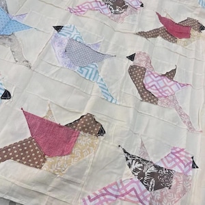 May include: A handmade quilt featuring appliqued birds in various patterns and colors. The birds are made from fabrics with polka dots, stripes, and floral designs. The background is a cream-colored fabric, and the birds have black beaks.