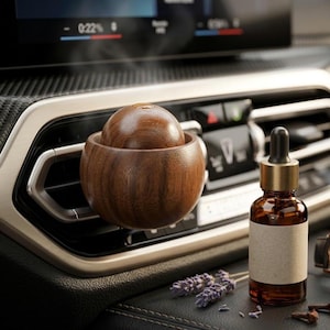 May include: A wooden car air freshener with a spherical design, resting in a car vent. A small amber glass bottle with a dropper and a blank label sits nearby, along with sprigs of lavender and cloves.