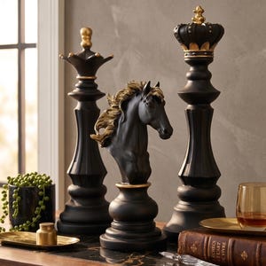 Three black chess pieces, a queen, knight, and king, with gold accents, stand on a dark wooden surface next to a potted plant and a glass.