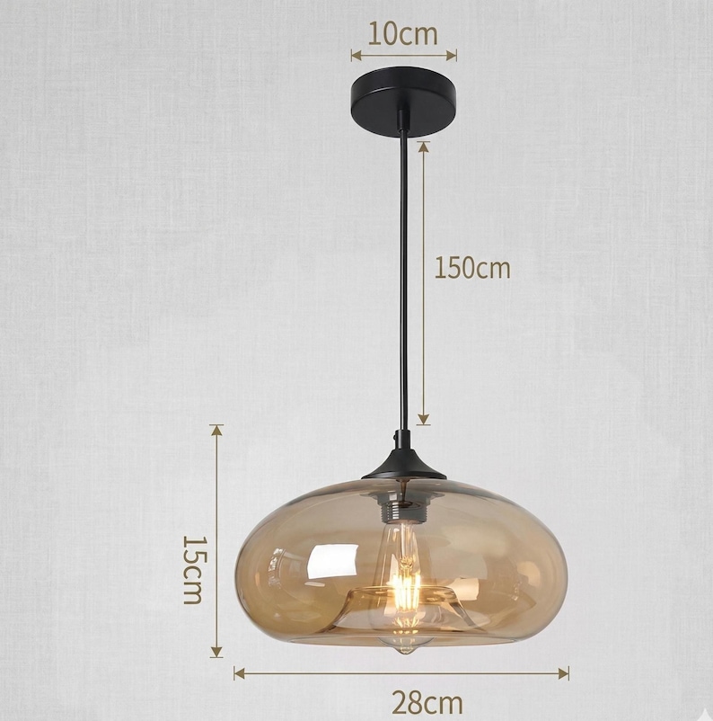Op de afbeelding: Een moderne hanglamp met een heldere, amberkleurige glazen kap. De lamp heeft een zwarte metalen basis en steel, met een totale hoogte van 150 cm. De kap is 28 cm breed en 15 cm hoog.