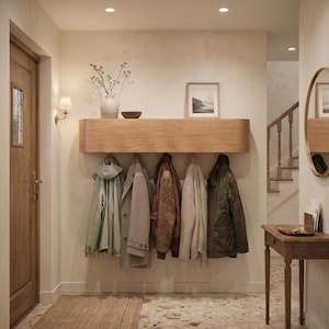 May include: A light oak wall-mounted coat rack with rounded edges features five hooks holding a light green hooded jacket, a grey wool coat, a brown leather jacket, a cream knit sweater, and a dark olive green utility jacket in a hallway.