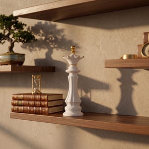 A white chess queen figurine with a gold crown is on a wooden shelf, with other shelves holding a bonsai tree, books, and a compass.