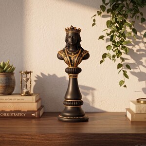 May include: A black and gold chess queen statue with a detailed bust, crown, and ornate collar. The statue is on a wooden surface with books, a succulent plant, and an hourglass. The words "ANTIQU&Eacute;S CHESS STRATEGY" are visible on a book.