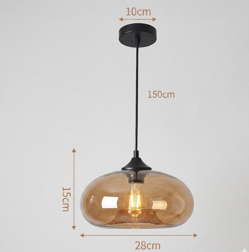 Op de afbeelding: Een moderne hanglamp met een bruine glazen kap, 28 cm breed en 15 cm hoog, hangend aan een zwarte stang. De plafondbevestiging heeft een diameter van 10 cm. De totale lengte van de lamp is 150 cm.