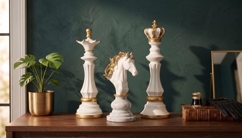 Three white chess pieces, a queen, knight, and king, with gold accents, stand on a dark wooden surface next to a green plant and a mirror.