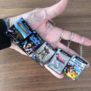 Peut inclure: Cinq porte-clés miniatures en forme de boîtiers de jeux Nintendo GameCube représentant Mario Kart Double Dash, Luigi's Mansion, Metroid Prime, The Legend of Zelda The Wind Waker et Super Smash Bros Melee, chacun fixé à un anneau en métal argenté.