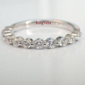 May include: A silver-toned band ring featuring a series of clear, round-cut stones set in a shared-prong arrangement along the top half of the band. The text RingVera is printed in red on the inner surface of the band, visible through the center.