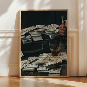 May include: A framed print showing piles of hundred-dollar bills on a dark wooden surface. A glass of amber liquid is placed nearby. The image evokes themes of wealth and finance.