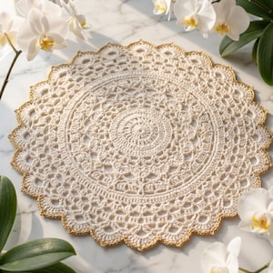 May include: A round, off-white crochet doily featuring an intricate, repeating lace pattern with a scalloped edge trimmed in metallic gold thread. The circular textile displays a dense, textured centre that transitions into an openwork design.