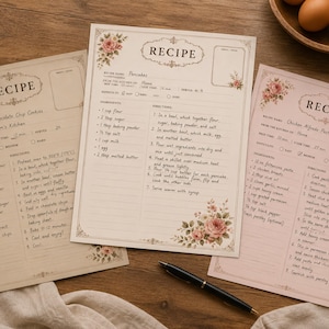 Könnte beinhalten: Drei rechteckige Rezeptkarten mit Blumenrändern und dem Wort RECIPE am oberen Rand. Jede Karte enthält handschriftliche Anleitungen und Zutatenlisten für Gerichte wie Pfannkuchen und Kekse, zusammen mit einem schwarzen Tintenstift auf einer Fläche.