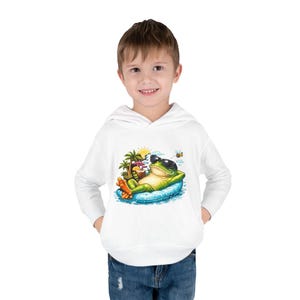 May include: White hooded sweatshirt featuring a cartoon frog wearing sunglasses and relaxing on a blue raft. The frog is holding a tropical drink, with palm trees and a sun in the background. A bee is flying nearby.