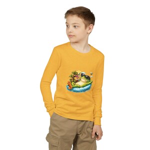 May include: Mustard yellow long-sleeve shirt featuring a graphic of a frog wearing sunglasses and relaxing on a float. The frog is holding a drink, with palm trees and a bee nearby. The shirt is made of a soft material.