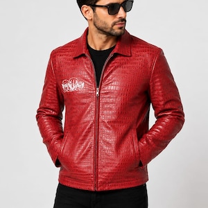 Puede incluir: Una chaqueta roja con un patrón texturizado de piel de cocodrilo, cuello clásico y cremallera frontal completa. La prenda presenta un diseño gráfico blanco en la parte superior derecha del pecho, mangas largas y dos bolsillos laterales.