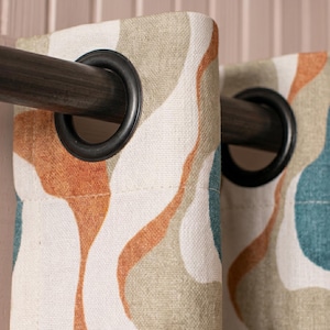 May include: A curtain panel featuring an abstract wavy pattern in shades of teal, burnt orange, and sage green on a cream background. The fabric is suspended from a dark metal rod by two large, circular black grommets at the top edge.