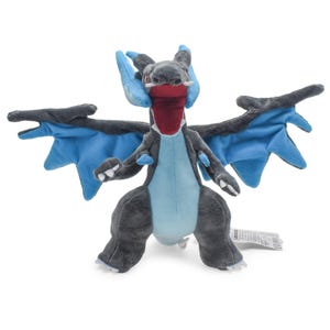 Könnte beinhalten: Ein Plüschtier in Form eines drachenartigen Wesens mit dunkelgrauem Fell, einem hellblauen Bauch und großen Flügeln mit leuchtend blauen Innenmembranen. Das Wesen hat ein weit geöffnetes, dunkelrotes Maul, kleine weiße Fangzähne und blaue Hörner.