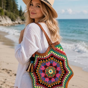 May include: A straw fedora hat with a black band and a red maple leaf patch, paired with a multi-colored crochet tote bag featuring a hexagonal mandala pattern, brown leather straps, and a decorative tassel hanging from the side.