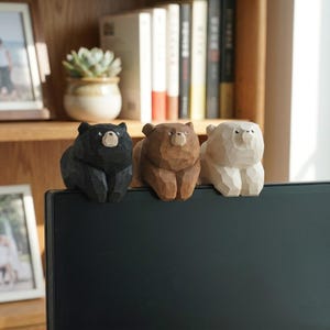 May include: Three wooden bear figurines in black, brown, and white sit atop a dark surface. The bears are carved with simple details, showcasing their distinct colors and textures. The figurines are a decorative item.