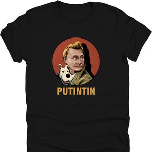 May include: Black t-shirt featuring a cartoon illustration of a man and a dog inside a red circle. The man has blond hair and is wearing a green jacket. The dog is white and black. The word "PUTINTIN" is printed in gold.
