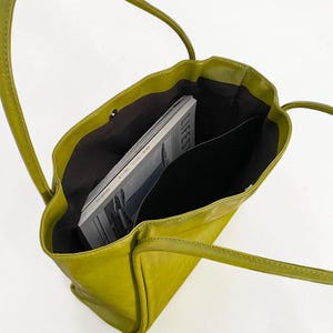 May include: A lime green tote bag with long handles. The bag is open, revealing a dark interior and a magazine with the word "LIFEST" visible. The bag appears to be made of a smooth, possibly leather-like material.
