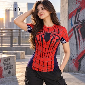 Pode incluir: Uma t-shirt de manga curta com um gráfico de teia de aranha vermelha e preta na frente, painéis laterais azuis e um padrão de favo de mel roxo e branco nas mangas. A peça é usada com calças cargo pretas num ambiente urbano ao ar livre.