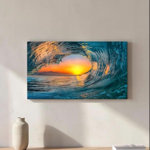 Può includere: Una stampa artistica rettangolare da parete che raffigura una grande onda oceanica che si infrange. Il centro dell'onda crea un'apertura circolare che rivela un vivace tramonto con tonalità arancioni, gialle e blu su un mare calmo e montagne.