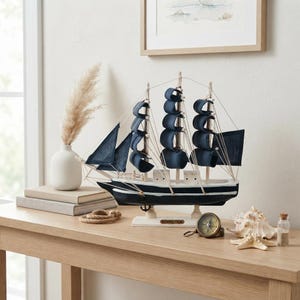 May include: A model sailing ship with a black and white hull and dark blue fabric sails. The ship features thin rigging lines, a small anchor, and a nameplate reading CONFECTION on the base. It is a decorative nautical piece.