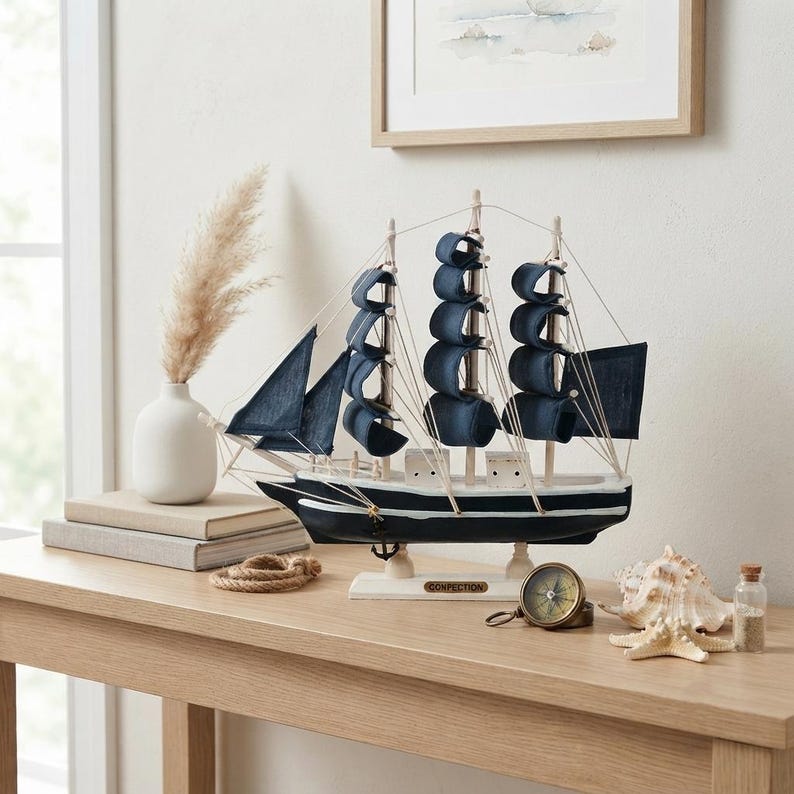 May include: A model sailing ship with a black and white hull and dark blue fabric sails. The ship features thin rigging lines, a small anchor, and a nameplate reading CONFECTION on the base. It is a decorative nautical piece.