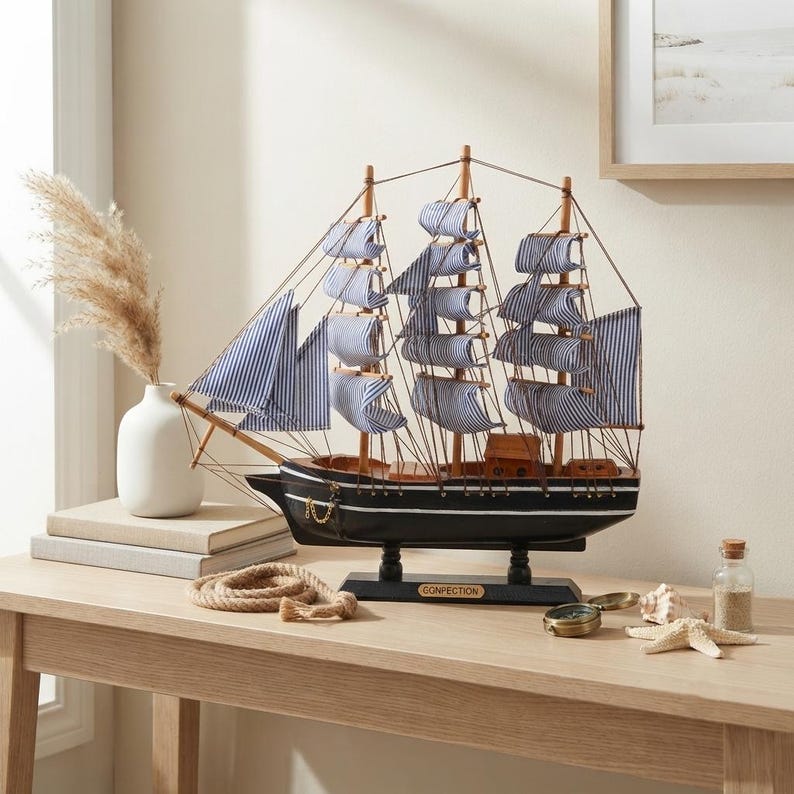 May include: A model sailing ship with a black hull, white horizontal stripes, and blue and white striped fabric sails. The ship features wooden masts, rigging, and a small plaque on the base labeled CONFECTION. It stands on a black pedestal.