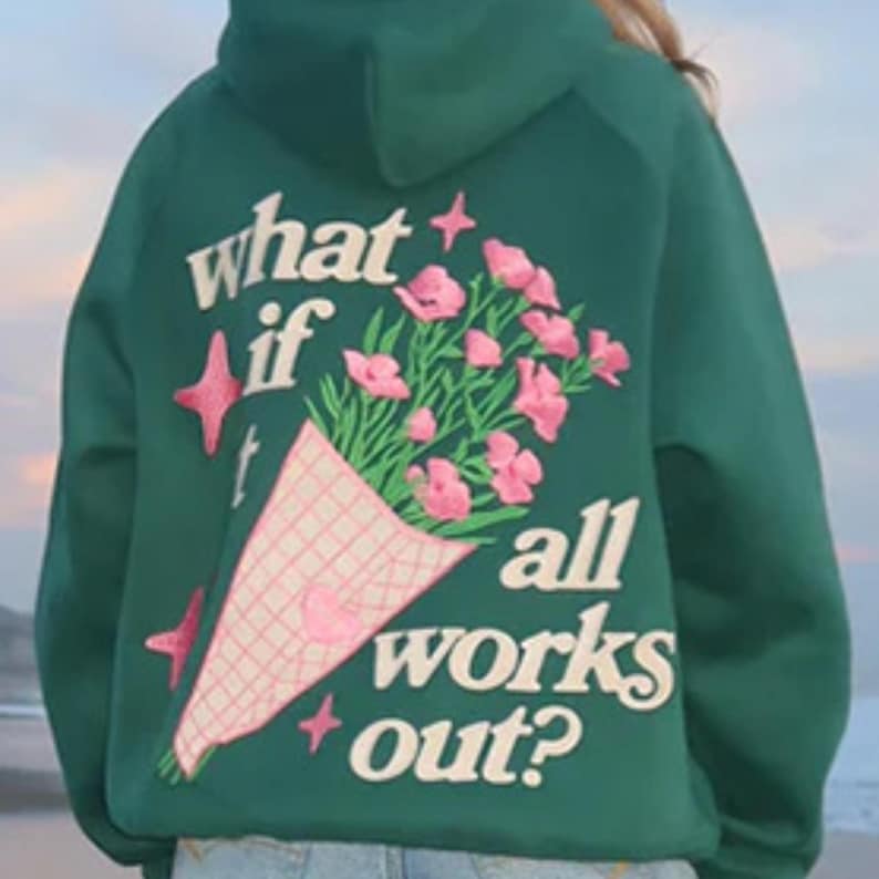 May include: Green hoodie with the phrase "what if all works out?" and a bouquet of pink flowers embroidered on the back. The bouquet is wrapped in a pink and white checkered paper. Pink star accents are also embroidered.