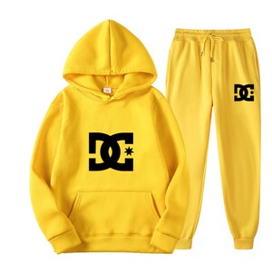 Peut inclure: Un ensemble jaune compos&eacute; d'un sweat &agrave; capuche et d'un pantalon de surv&ecirc;tement assorti. Le sweat &agrave; capuche a une capuche, une poche avant et un logo noir sur le devant. Le pantalon de surv&ecirc;tement a une taille &agrave; cordon et un logo noir sur la jambe.