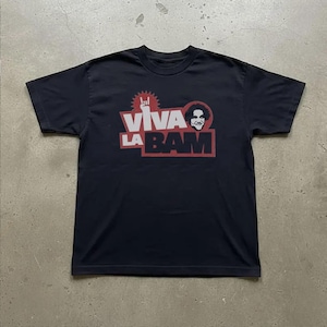 Peut inclure: Un t-shirt noir à manches courtes avec une impression graphique sur la poitrine. Le motif comprend le texte VIVA LA BAM en lettres blanches et noires, une forme d'étoile rouge, une main blanche faisant un geste rock et un portrait circulaire.