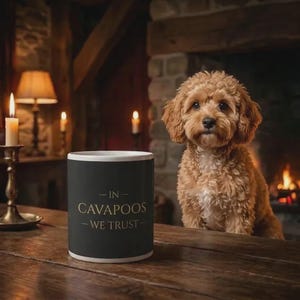 May include: A black mug with white trim displays the gold text "- IN - CAVAPOOS - WE TRUST -". A light brown Cavapoo dog is positioned near a fireplace. The scene is lit by candles and a warm fire.
