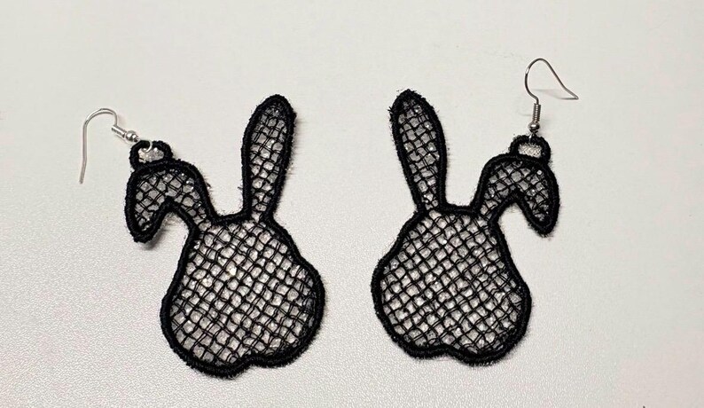 May include: A pair of black lace bunny-shaped earrings. The earrings feature a delicate, open-weave design, with a bunny silhouette. The earrings have silver-colored ear wires. The earrings are displayed on a white surface.
