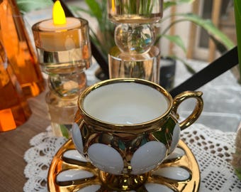 Juego de taza y platillo de porcelana con silueta floral y detalles dorados.