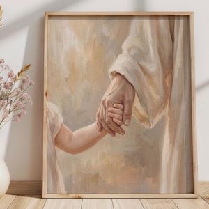 May include: Framed artwork depicting a person's hand holding a child's hand. The painting features soft, warm tones of beige and cream, with a focus on the connection between the hands. The artwork is displayed in a light wooden frame.