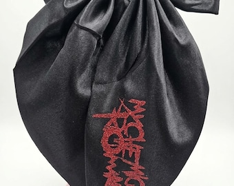 May include: A large black satin hair bow featuring a smooth, shiny finish. The fabric is folded into a structured, multi-layered bow shape. On the lower right tail, the text My Chemical Romance is written in a stylised, glittery red font.