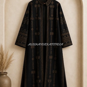 May include: A long-sleeved black open-front coat featuring a mandarin collar and intricate gold-toned embroidery in floral and geometric patterns. The garment displays the text ASSUHANDICRAFTINDIA across the centre and hangs on a wooden hanger.