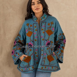 Könnte beinhalten: Eine blaue Jacke mit aufwendigen Blumenstickereien in Orange-, Rosa- und Violetttönen. Das Kleidungsstück hat einen Stehkragen, lange Ärmel und zwei Vordertaschen. Der Text ASSUHANDICRAFTINDIA ist in der Mitte der Jacke zu sehen.