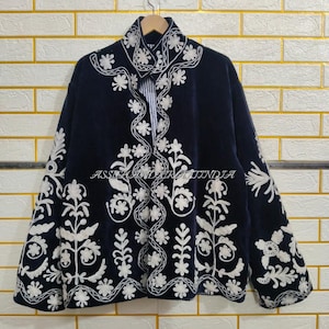 Könnte beinhalten: Eine dunkelmarineblaue Jacke mit aufwendiger weißer Blumenstickerei auf der Vorderseite und den Ärmeln. Das Kleidungsstück hat einen hohen Kragen, lange Ärmel und ein sichtbares weiß-blau gestreiftes Futter an der vorderen Öffnung.