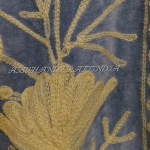 May include: A blue fabric featuring intricate yellow floral embroidery with stems and leaves. The text ASSUHANDICRAFTINDIA is embroidered in the center. The design displays a large central flower with smaller buds and foliage extending upwards.