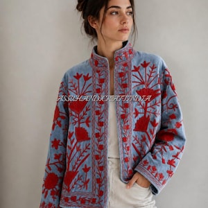 May include: A light blue jacket featuring vibrant red floral embroidery throughout the front panels and sleeves. The garment has a high collar, long sleeves, and an open front design. The text ASSUHANDICRAFTINDIA is visible across the center.