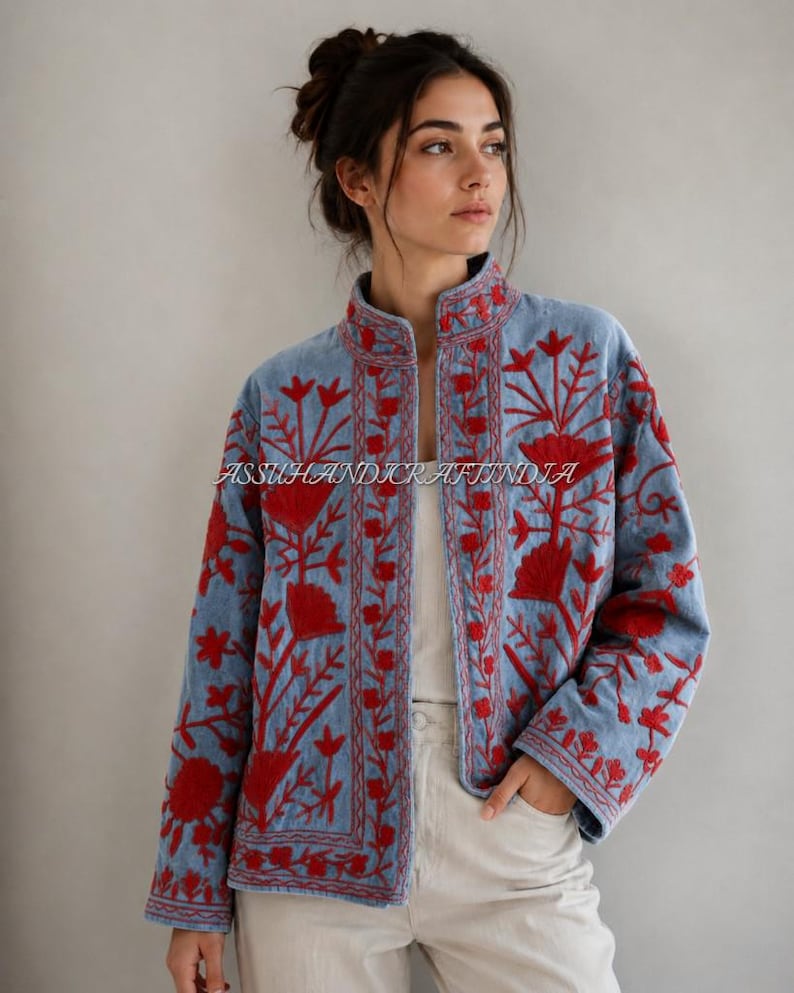May include: A light blue jacket featuring vibrant red floral embroidery throughout the front panels and sleeves. The garment has a high collar, long sleeves, and an open front design. The text ASSUHANDICRAFTINDIA is visible across the center.