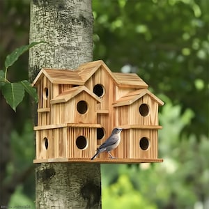 Puede incluir: Un pajarera de madera de varios niveles con múltiples orificios de entrada circulares y tejados a dos aguas. La pajarera está montada en un tronco de árbol, y un pequeño pájaro gris está posado en el borde.