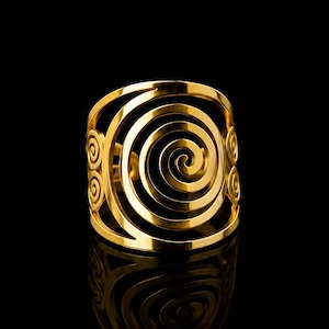 Peut inclure: Un bracelet manchette doré avec un motif en spirale. Le bracelet présente des spirales concentriques, créant une esthétique ouverte. Le métal reflète la lumière, soulignant les détails complexes. Un bijou de caractère, adapté à diverses occasions.