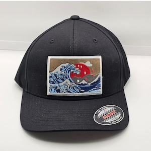 Peut inclure: Casquette de baseball Flexfit noire avec un écusson rectangulaire représentant une vague japonaise bleue, blanche et rouge. La casquette a une visière incurvée et un autocollant Flexfit.