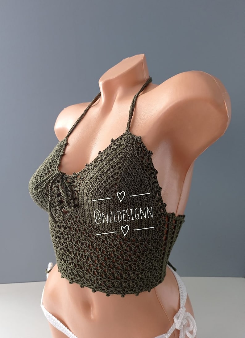 Pu&ograve; includere: Un top halter in crochet verde con un motivo delicato. Il top &egrave; legato al collo e alla schiena. Il top &egrave; mostrato su un manichino. Il testo "@NZLDESIGNN" &egrave; scritto sul top.