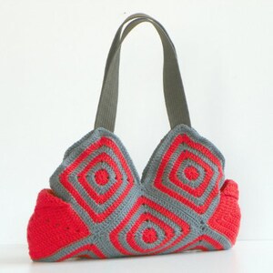 May include: A gray and red crocheted tote bag with a geometric pattern. The bag has two straps and a wide base.