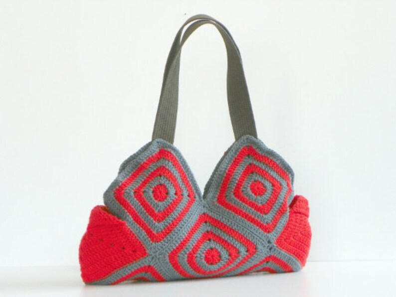 May include: A gray and red crocheted tote bag with a geometric pattern. The bag has two straps and a wide base.