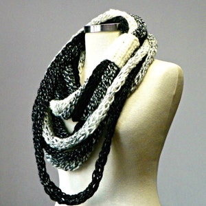 May include: A black and white infinity scarf made of chunky yarn. The scarf is looped around a white mannequin's neck.
